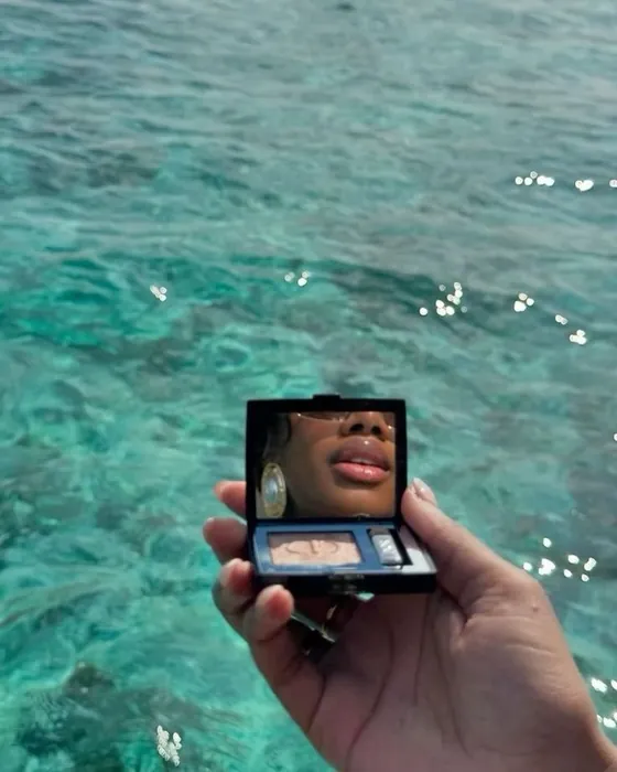 Hand holding an open compact mirror above turquoise water
