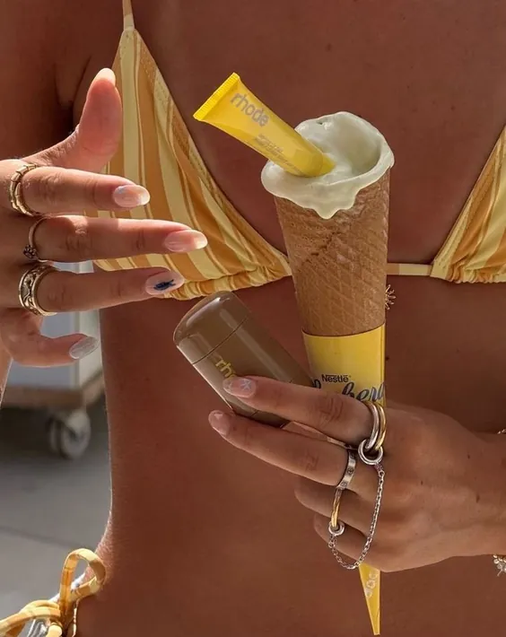 Hands holding an ice cream cone and a yellow sunscreen tube on the beach